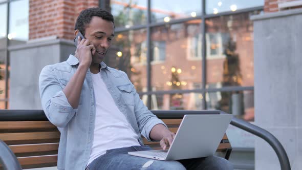 African Man Talking on Phone, Sitting on Bench alt