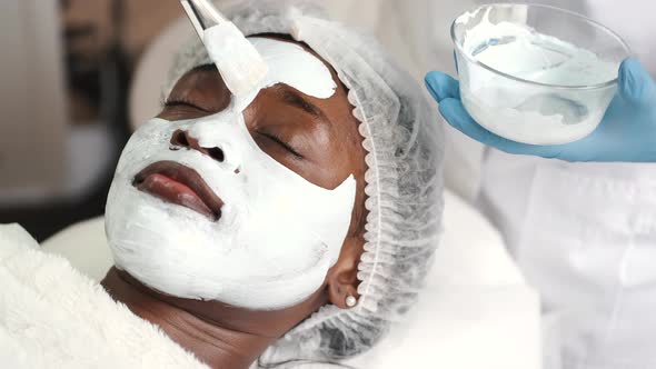 Cosmetologist Applies Alginate Mask with Spatula on Face of Woman alt