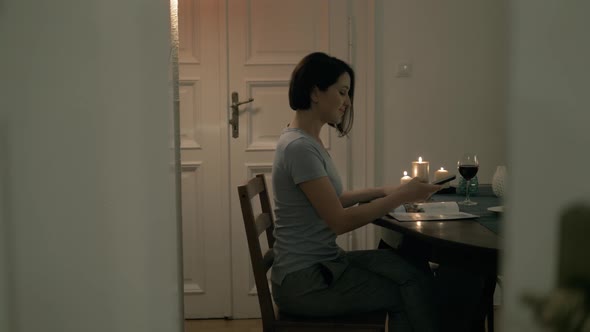 Happy Young Woman Smiling Using Her Smart Phone While Drinking Wine at Home alt