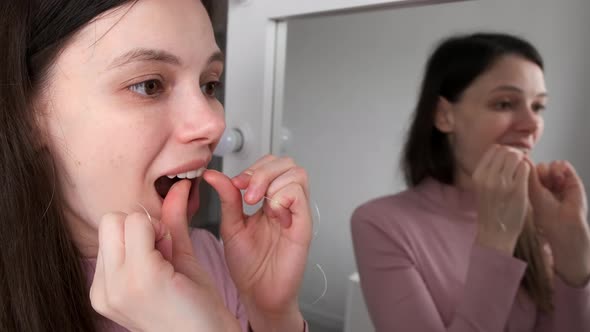 Portrait of Young Woman is Cleaning Teeth with Dental Floss Smiling in Bathroom