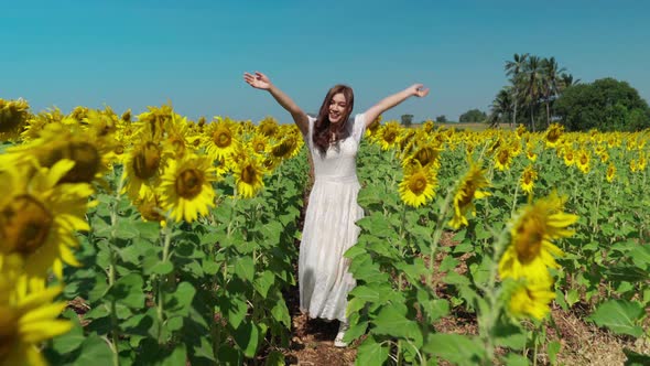 cheerful woman walking with arms raised and enjoying with sunflower field
