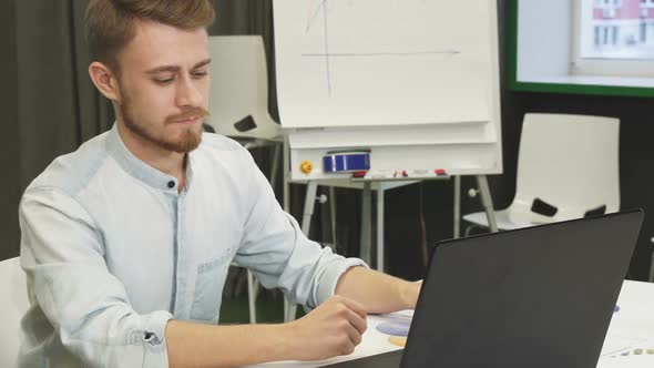 Attractive Young Man Using His Smart Phone and Laptop at the Office alt