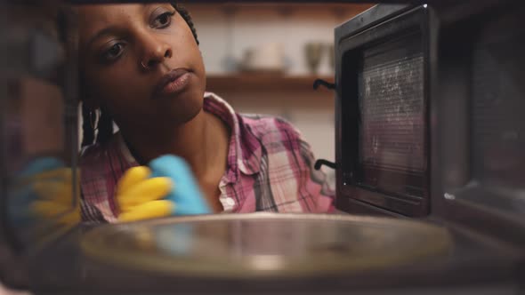 African Woman Leaning Microwave Oven with Sponge and Detergent Spray