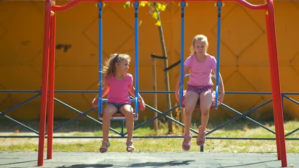 Two girls ride a swing in the Park on a Playground on a summer day