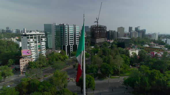Orbital footage left to right around mexican flag with view of an principle avenue in Mexico City at alt