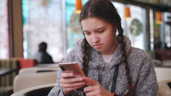 Teenage Girl Texting on Smartphone Sitting in Cafe alt
