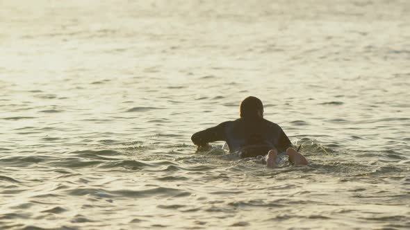 Rear view of mid-adult caucasian male surfer swimming in sea during sunset 4k alt