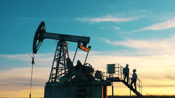 Two Workers Are Talking While Standing on a Pumpjack alt