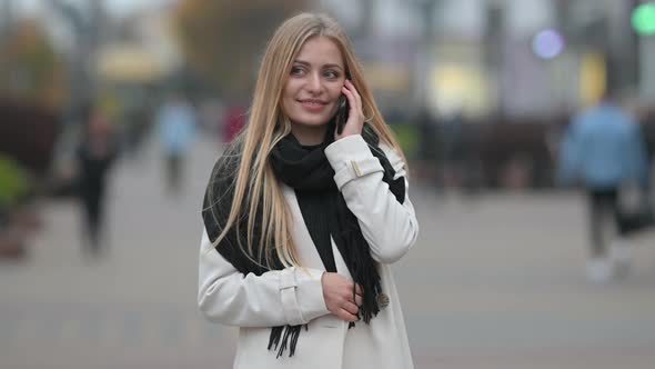 beautiful young blonde girl in a coat communicates on the phone alt