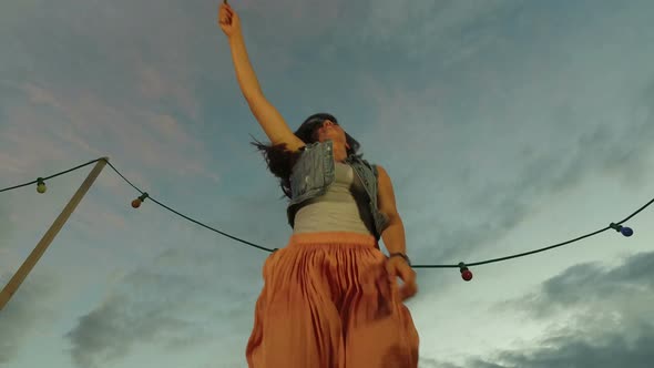 Low angle view of woman jumping with firework candle on rooftop terrace alt