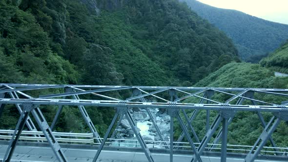 Aerial view of metal bridge over narrow rocky valley with the river alt