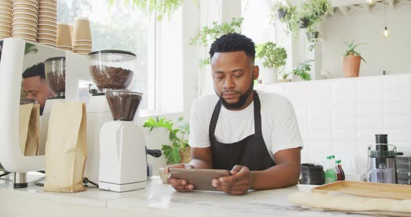 African american male cafe owner standing by counter using tablet at cafe alt