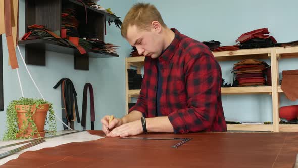 Young Male Craftsman Marks on the Leather Cloth Using a Ruler and an Awl. Handmade Manufactures alt