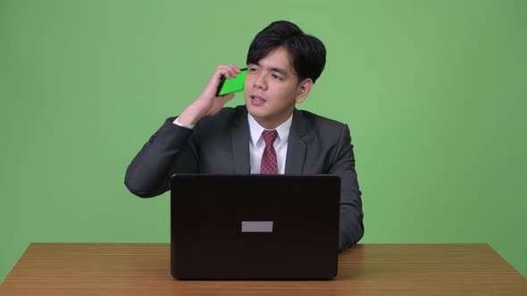 Young Handsome Asian Businessman Working with Laptop Against Green Background alt