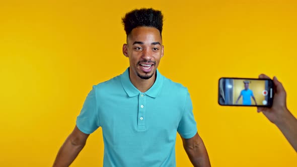 Smiling African Blogger Man Making Online New Video Blog, Vlog, with His Smartphone on Yellow alt