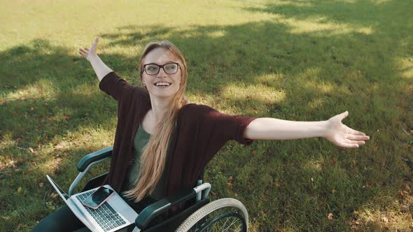 Happy Young Disabled Caucasian Woman in the Wheelchair Resting in the Nature with Laptop and alt
