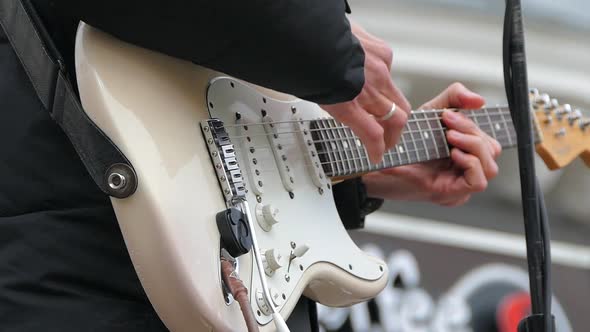 A Man Plays on Electric Guitar Strings with a White Body