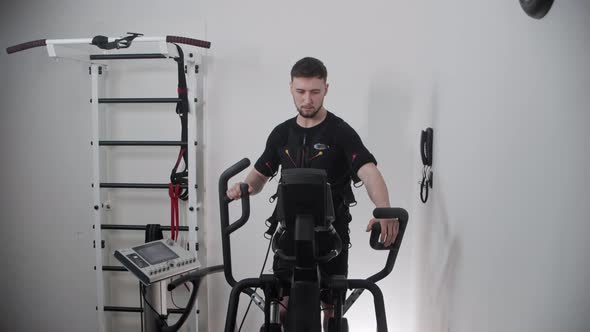 A Man Wearing Electrostimulation Suit and Training on Exercise Bike alt