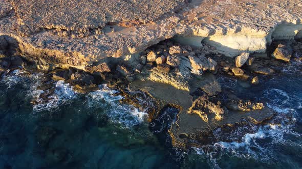Flying Over Rocky Coastline Alongside Cliffside with Blue Mediterranean Sea Ocean Water Towards the alt