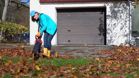 Housekeeper Woman with Leaf Blower Cleaning Path From Colorful Autumn Leaves