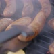 Hand with the Help of Metal Tongs Turns the Simmering Sausages on a Black Barbecue Grill - VideoHive Item for Sale