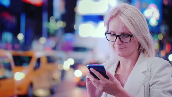 A Young Woman Uses a Smartphone on a Busy Street in Manhattan Against the Backdrop of Bright alt