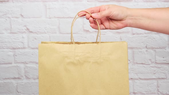female hand puts brown paper bag with handles for shopping and products alt