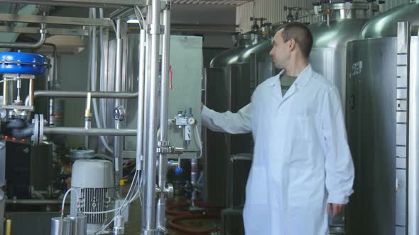 A Man in a White Coat at the Brewery Sets Up Equipment for Beer Production