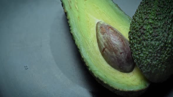 Two Halves of an Avocado Rotate in a Circle on a Black Background alt
