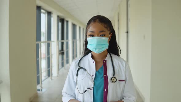 Young African American Doctor Woman in a Blue Suit and White Coat Wears a Disposable Sterile Face alt