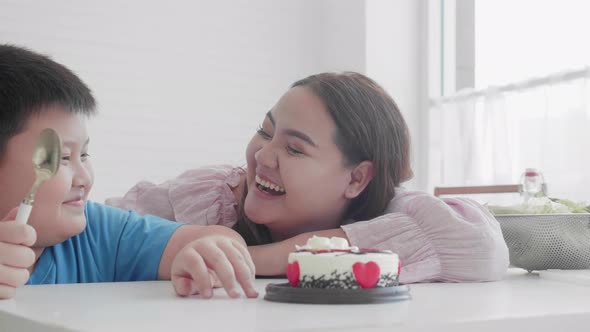 Asian family relationship with son feeding cake with mother in birthday and hug at home. alt