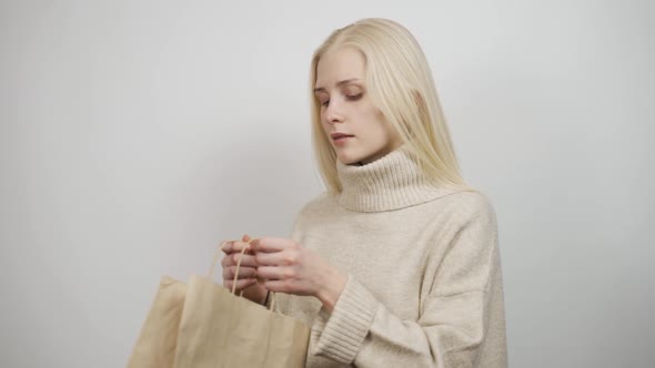 A Young Woman in a Cozy Sweater Opens the Package is Surprised and Happy with the Gift