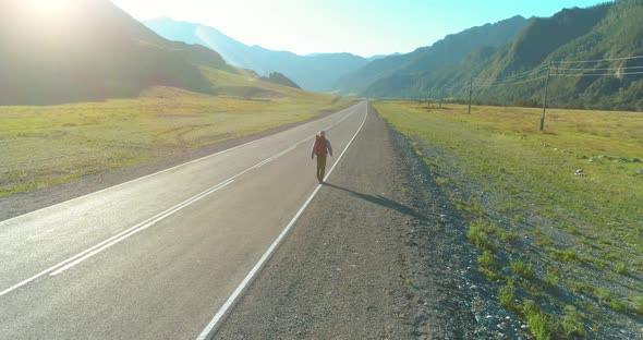 Flight Over Hitchhiker Tourist Walking on Asphalt Road. Huge Rural Valley at Summer Day. Backpack alt