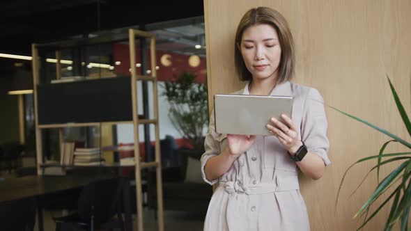 Asian businesswoman standing using a digital tablet in a modern office alt
