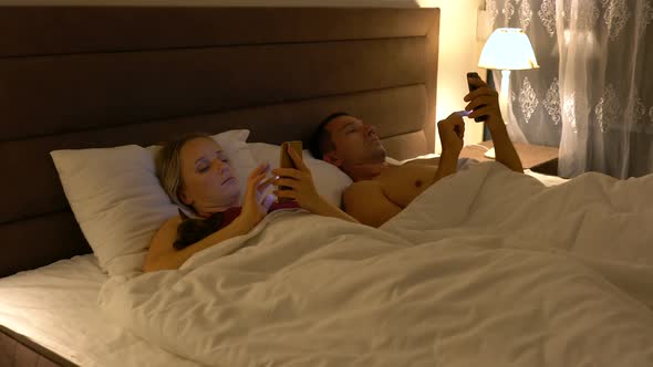 Couple Lies in Bed and Use Smartphones