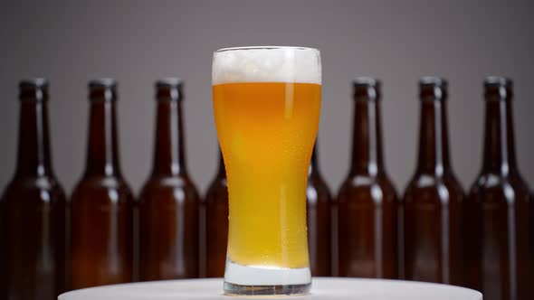 Glass with beer and foam rotates against the background of bottles