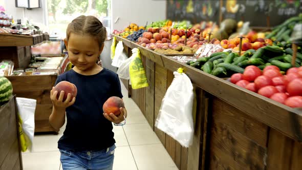 Kid Girl with Two Peaches Is Walking Along Grocery Rows Toward To Cashier alt