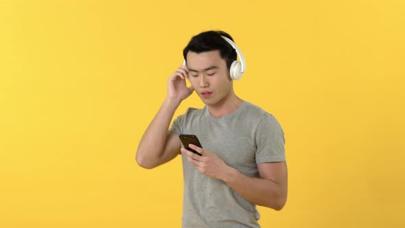 Young  Asian man wearing headphones while listening to music from smart phone