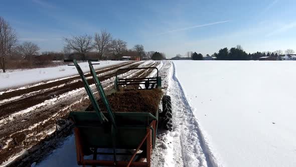 Agricultural Machinery Is Being Pulled To Spread Manure On Farmland During Sunny Winter Day. - Track alt