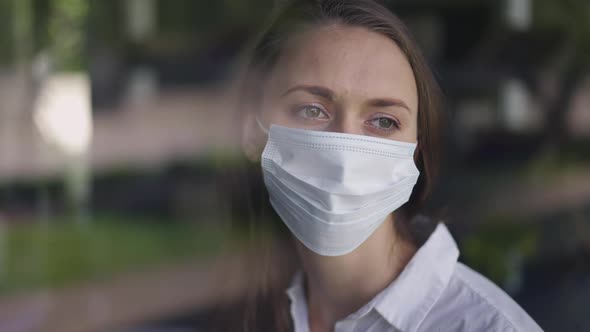 Closeup Portrait of Caucasian Sad Woman in Covid19 Face Mask Looking Out the Window Thinking alt