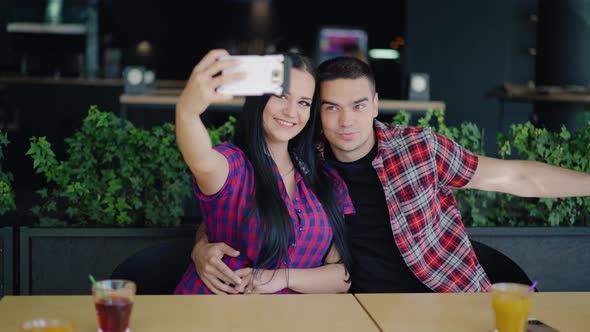 Loving Couple in a Playful Mood are Taking a Selfie at the Table in the Cafe  alt