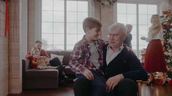 Boy Sitting on a Chair with His Grandad and Talking at Christmas Celebration alt