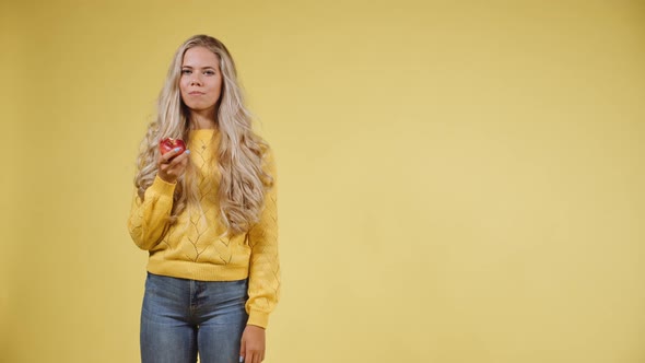 Hungry Woman with Long Blonde Hair Eating an Apple with a Smile on Her Face alt