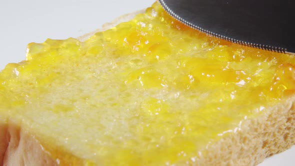 Human hand smears a apricot jam on a bread slice by a knife