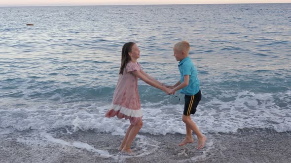 Little Brother and Sister Having Fun on the Beach They Hold Hands and Jump alt