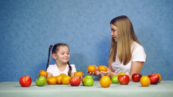 Woman and little girl playing with fresh fruits at home alt