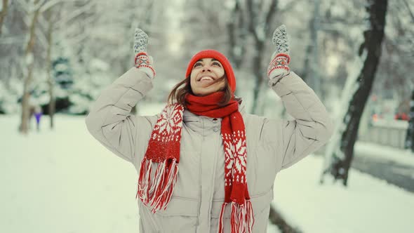 Cheerful Smiling Woman in Warm Clothes Red Knitted Cap Scarf and Mittens Stands in Snowy Park alt