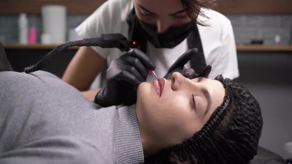 Cosmetologist Applies a Permanent Makeup to the Lips of a Caucasian Client with a Needle with a alt