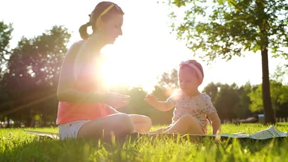 Little baby girl sitting with her mother on green grass in summer.