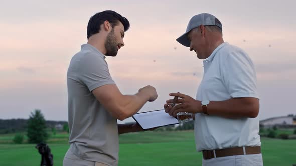 Two Golfers Communicate Outside on Sunset Fairway alt
